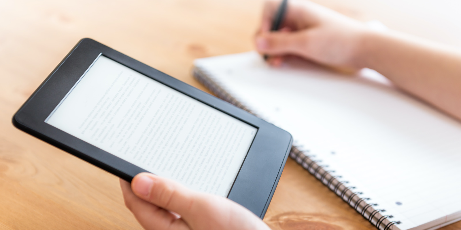 an individual reading a cybersecurity eBook on a tablet and taking notes