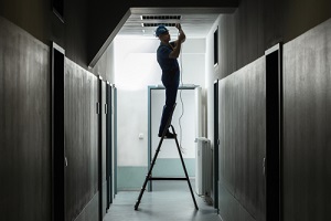 Male Electrician On Step Ladder Installing Light At Corrido