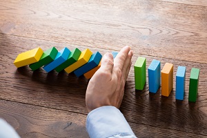 person hand stopping falling dominoesf from continuous toppled