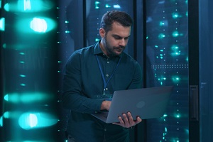professional admin using laptop computer doing data transfer operation with rack server cabinets in digital room of data center