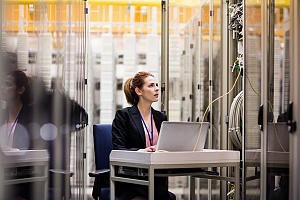 woman sitting at a work station in a server room to perform it security checks